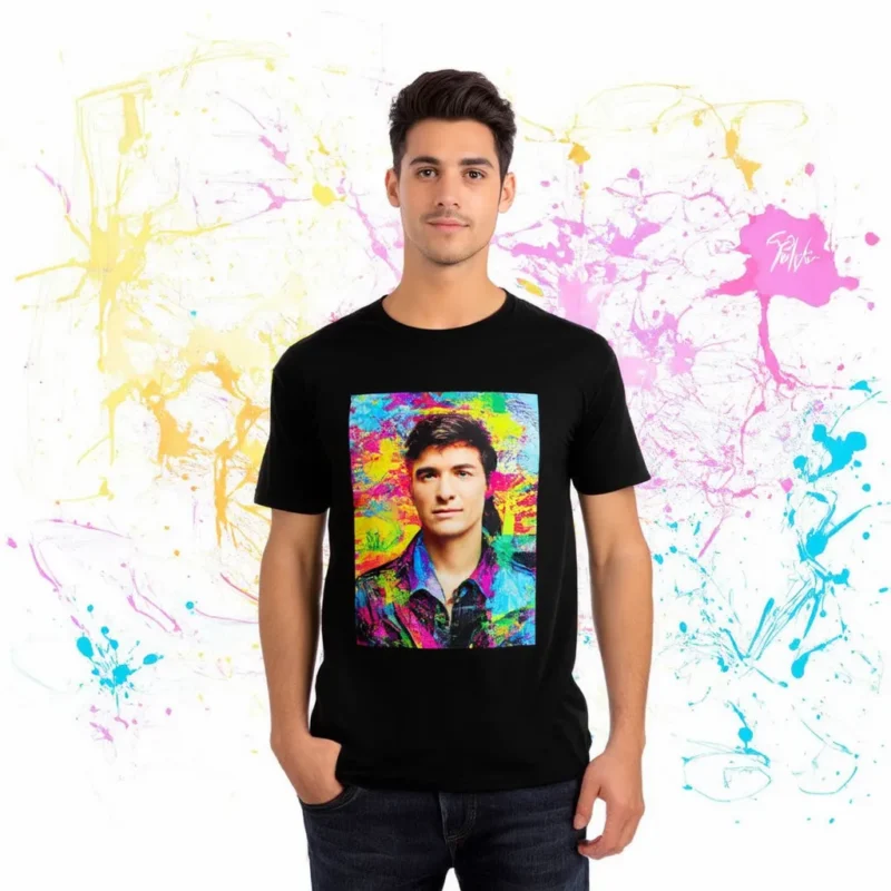 A man wearing a black T-shirt with a vibrant, colorful portrait print stands against a background of splattered pastel paint.