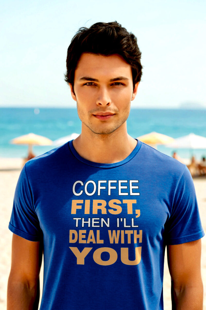 Young man in a blue T-shirt with the text “Coffee First, Then I’ll Deal With You,” standing on a beach.