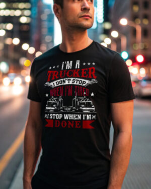 Man wearing a black T-shirt with the slogan “I’m a Trucker – I Don’t Stop When I’m Tired, I Stop When I’m Done” and two truck graphics, standing on a city street at night.
