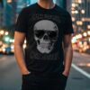 Man wearing a black T-shirt with a skull in sunglasses and the phrase “Drink Cold Beer in the Afterlife,” standing on a city street at night.
