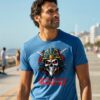 Man in a blue T-shirt with a samurai skull illustration and text “Honor in the Shadows,” walking along a beachfront promenade.