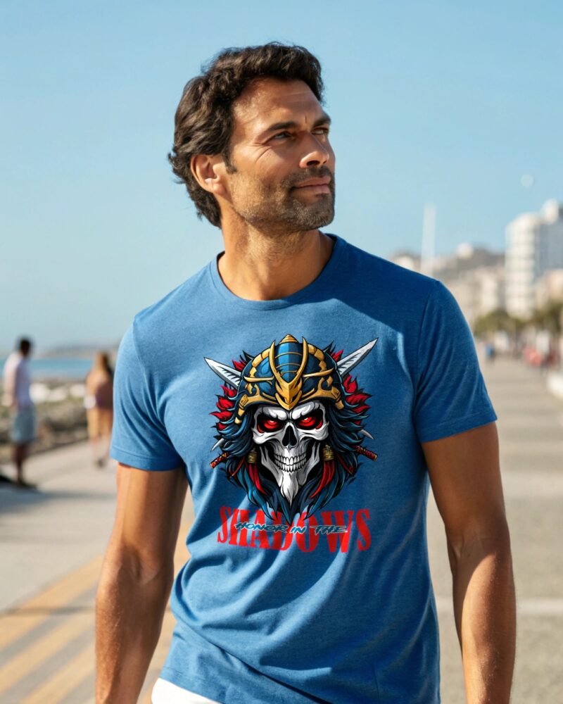Man in a blue T-shirt with a samurai skull illustration and text “Honor in the Shadows,” walking along a beachfront promenade.