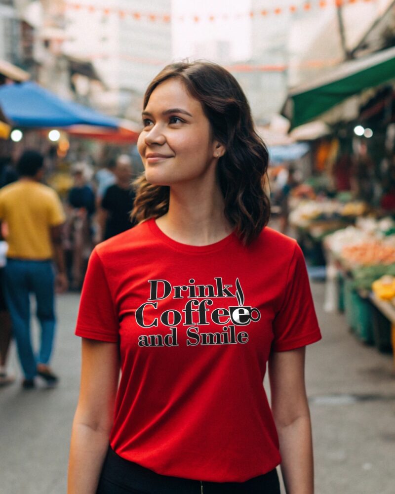 Smiling young woman in a red T-shirt with the quote “Drink Coffee and Smile,” walking through a vibrant outdoor market.