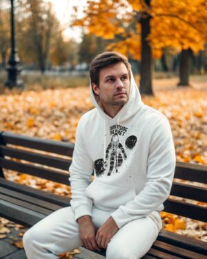 Man in a white hoodie with a black astronaut design and the phrase “Think Outside the Planet,” sitting on a bench in an autumn park surrounded by fallen leaves.