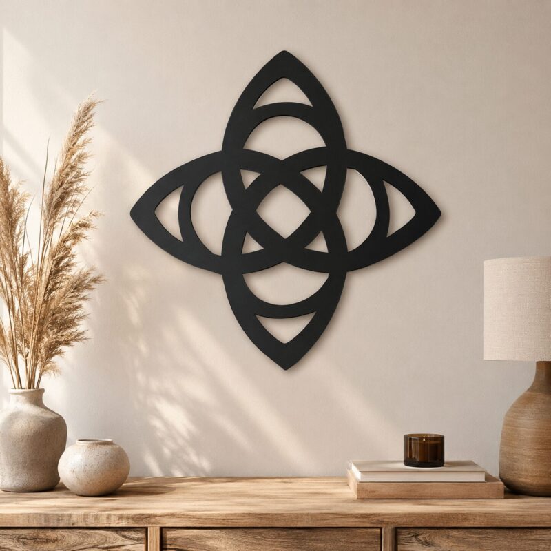 Black Celtic Trinity Knot wall decor displayed on a neutral wall above a wooden console with ceramic vases, dried grasses, books, candle, and lamp.