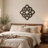 Black Celtic knot wall decor displayed above a wooden bed in a warm neutral bedroom with cream bedding, wooden nightstands, greenery, and soft lighting.