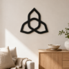 Black triquetra Celtic knot wall decor displayed in a warm neutral living room above a wooden cabinet.