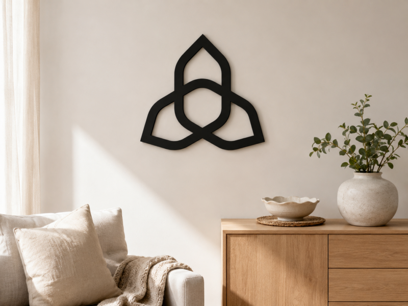 Black triquetra Celtic knot wall decor displayed in a warm neutral living room above a wooden cabinet.